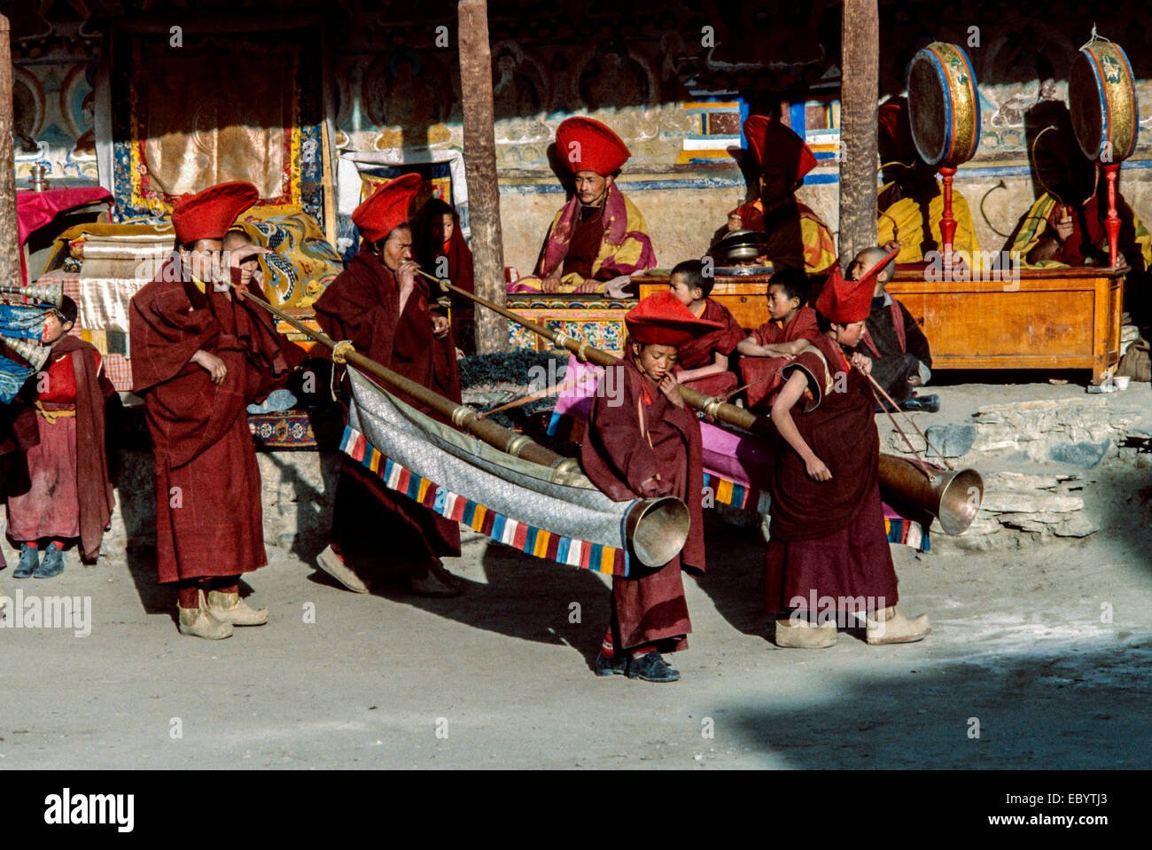 Monks wearing red hats and gonchas play traditional Tibetan Buddhist brass long horns in a monastery courtyard in Ladakh India Stock Photo