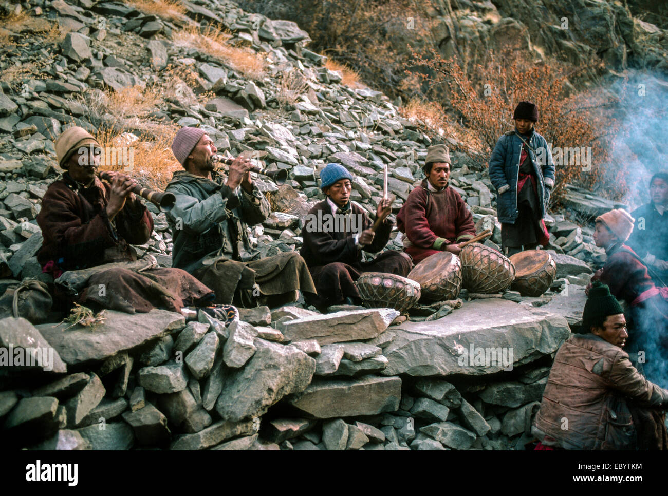 Local village musicians of low cast sit and play their clarinets and drums against a rocky backdrop in Ladakh India Stock Photo