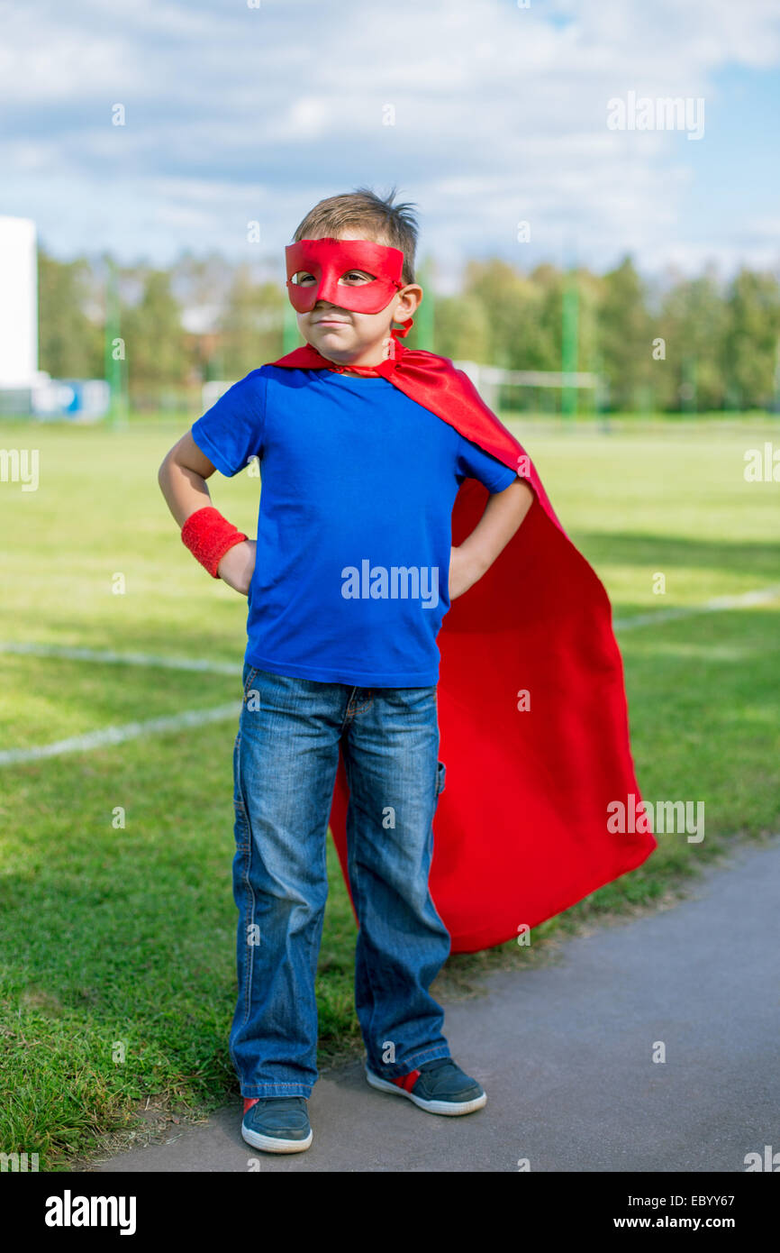 Boy dressed in cape and mask standing with hands on hips and looking towards Stock Photo
