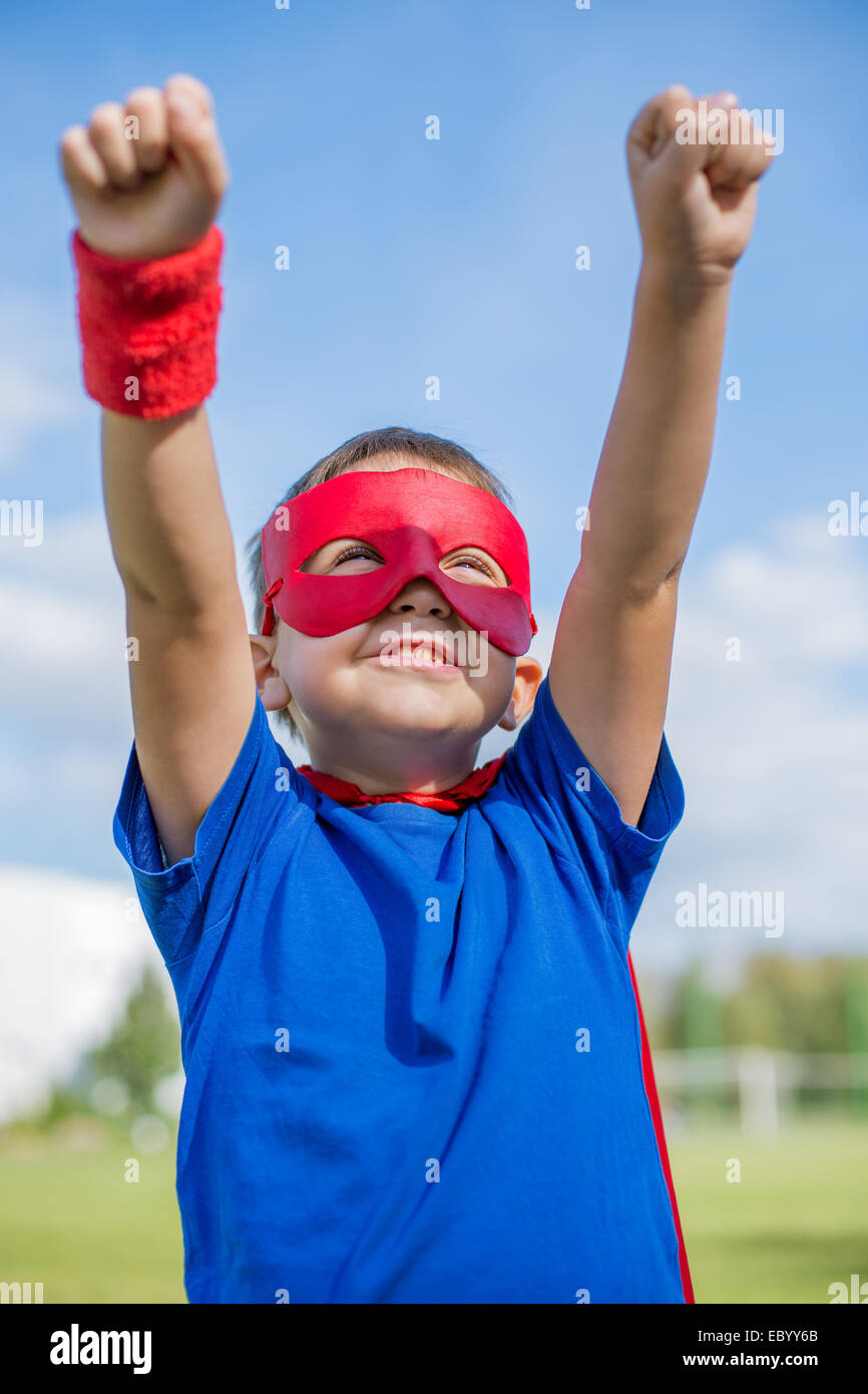 Boy dressed in cape and mask holding hands up and looking at the sun Stock Photo