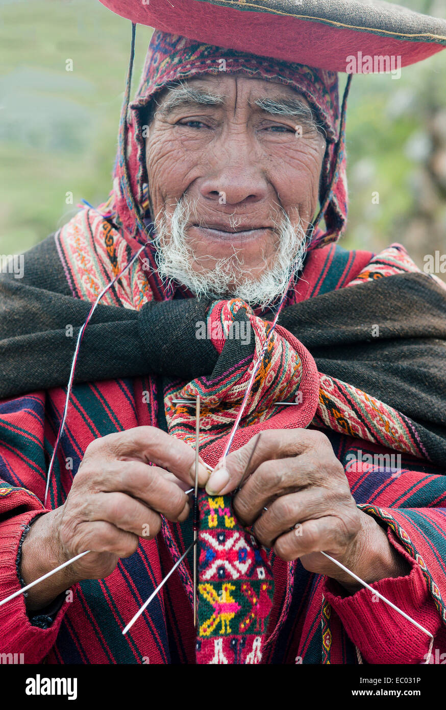 Elderly Quechua man in traditional dress and hat knits a complicated ...