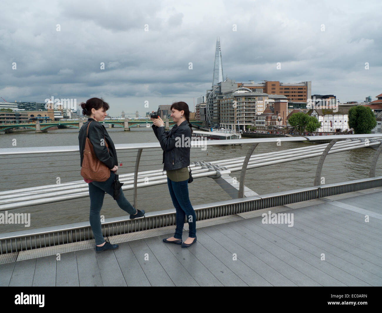 A young woman photographing her friend on the Millennium Bridge over the River Thames in London UK  KATHY DEWITT Stock Photo