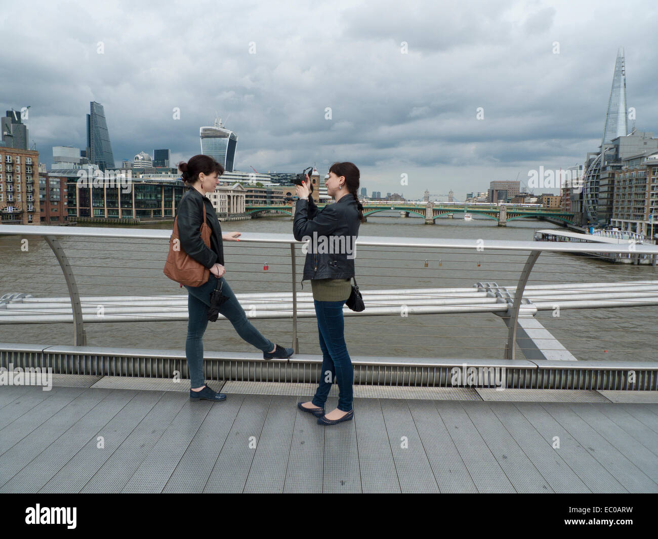 A young woman photographing her friend on the Millennium Bridge over the River Thames in London UK  KATHY DEWITT Stock Photo