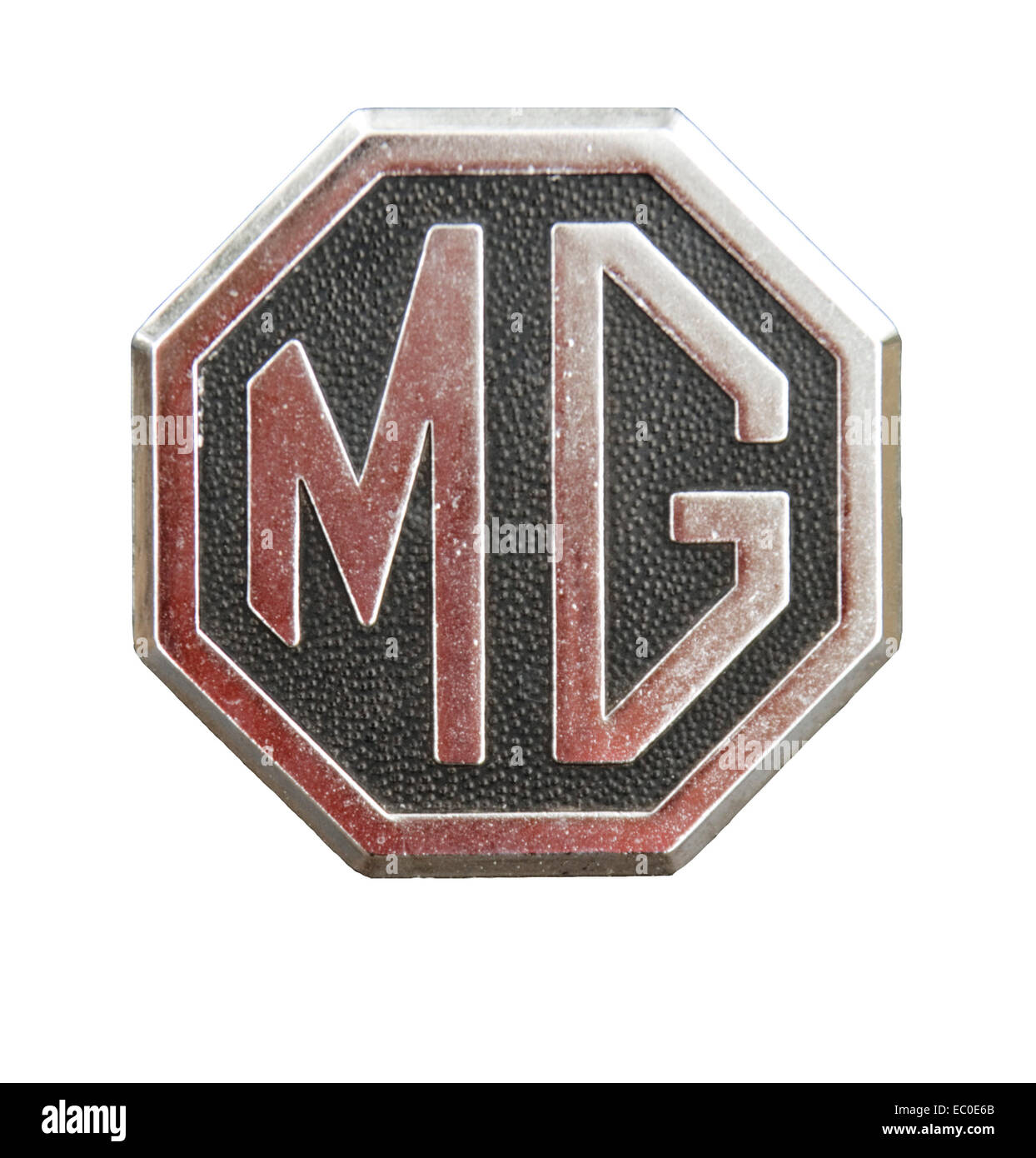 Octagonal metallic MG car emblem, large dark red letters on stippled black finish with red border, on plain white background Stock Photo