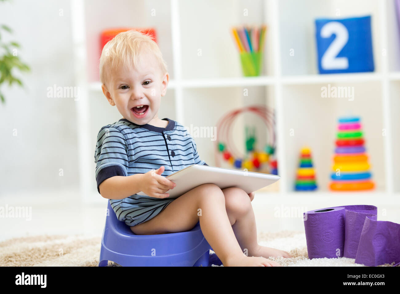 child sitting on chamber pot playing tablet pc Stock Photo