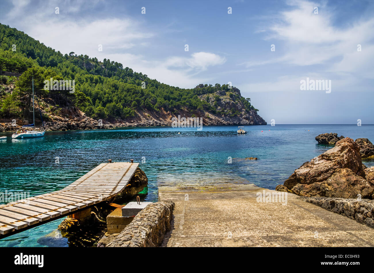 Launching ramp into the sea for small yachts and boats along side a wooden jetty with forest background on a promontory. Stock Photo