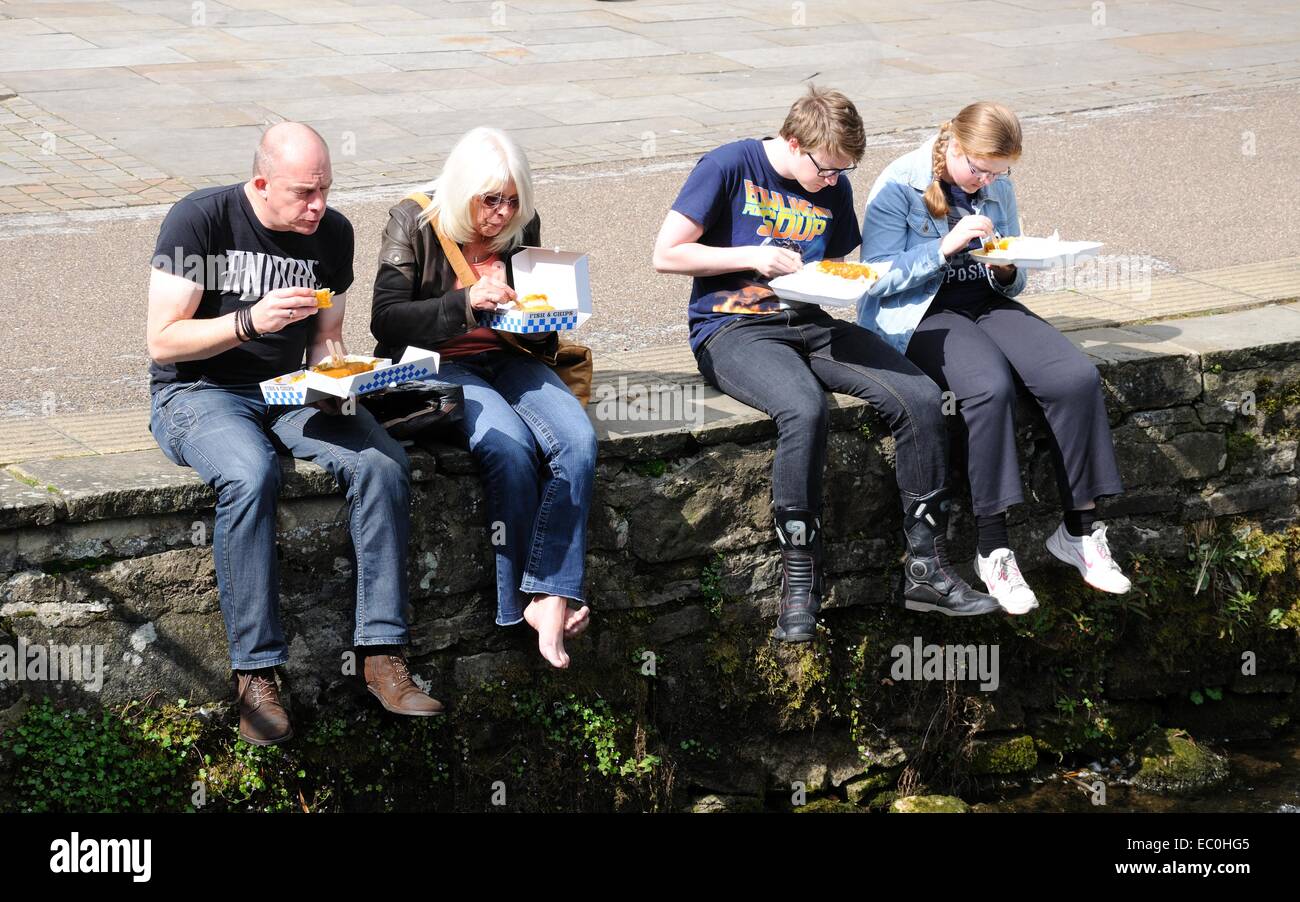 Family sitting on the riverbank eating fish and chips, Bakewell