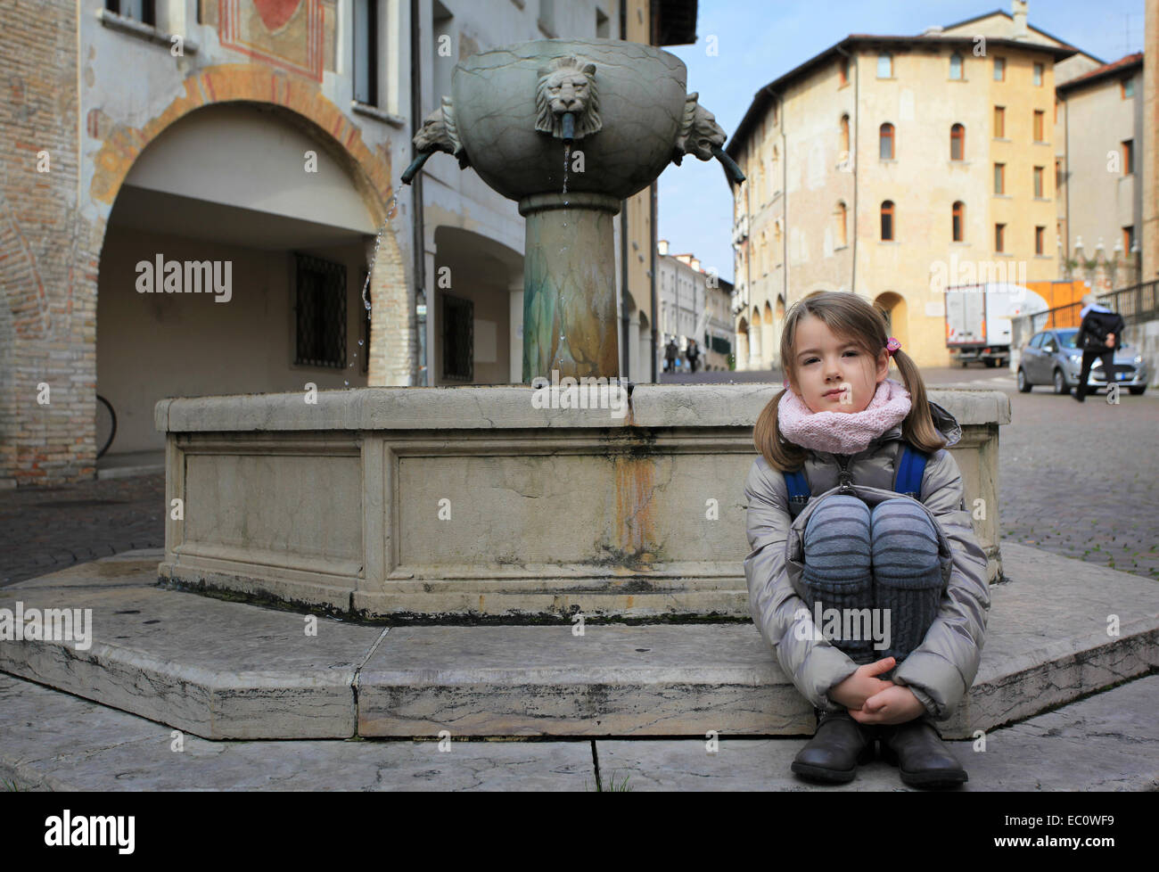 A little girl lingering at the fountain in Piazza San Marco, a square in the historical city center of Pordenone, Italy. Stock Photo
