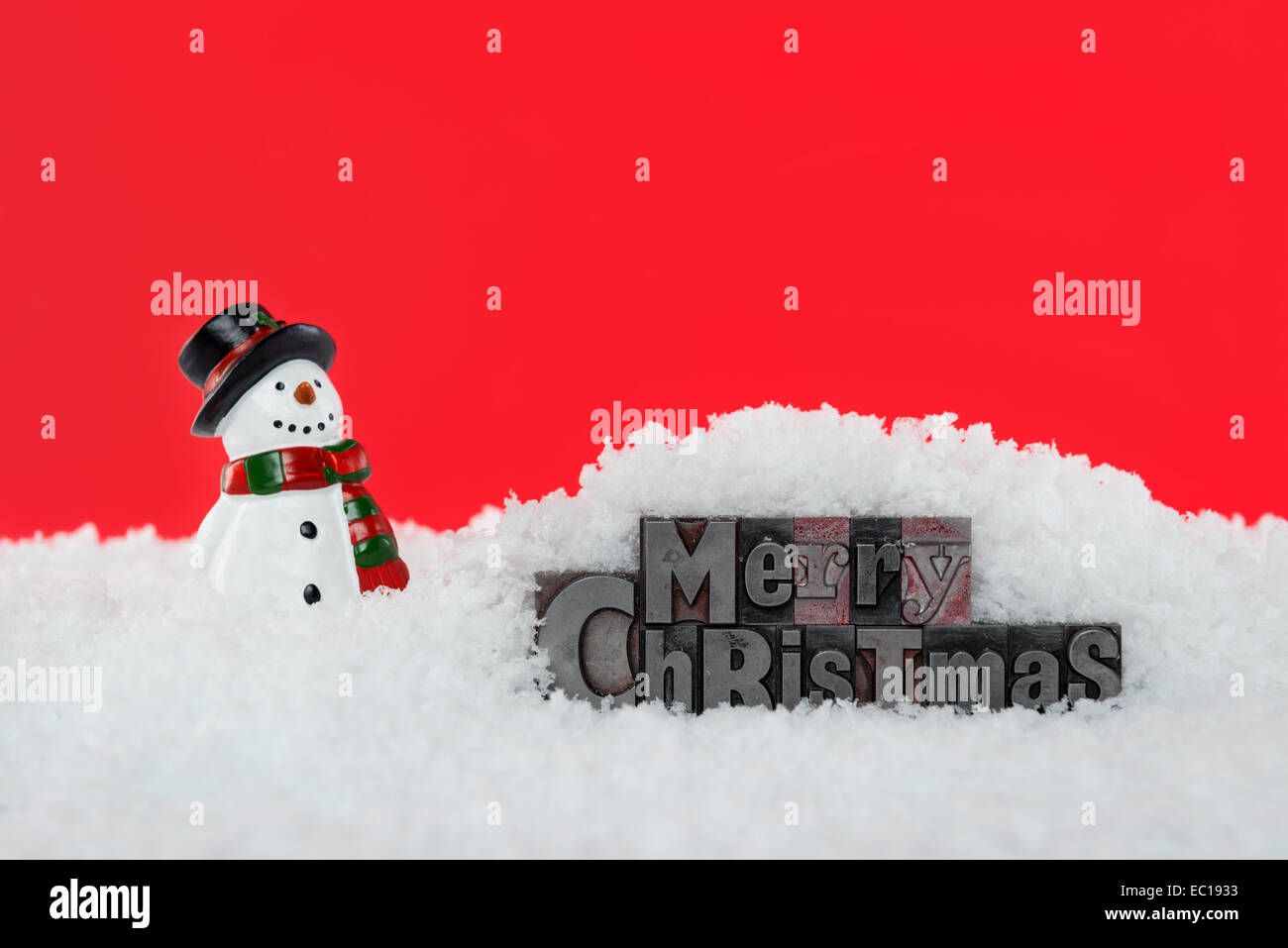 The words Merry Christmas in old letterpress surrounded by snow and a snowman, red background. Stock Photo