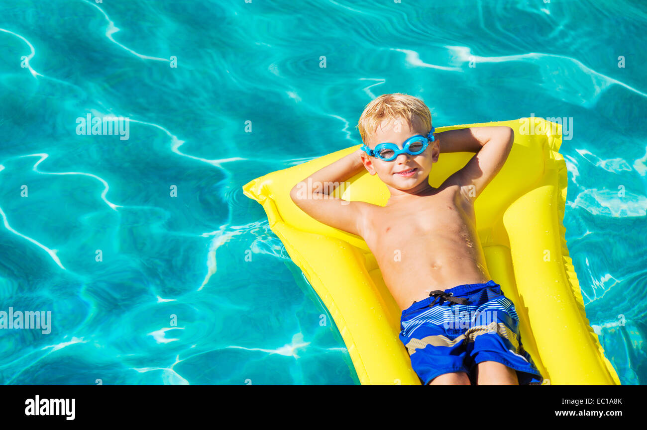 Young Boy Relaxing and Having Fun in Swimming Pool on Yellow Raft. Summer Vacation Fun. Relaxing Lifestyle Concept. Stock Photo