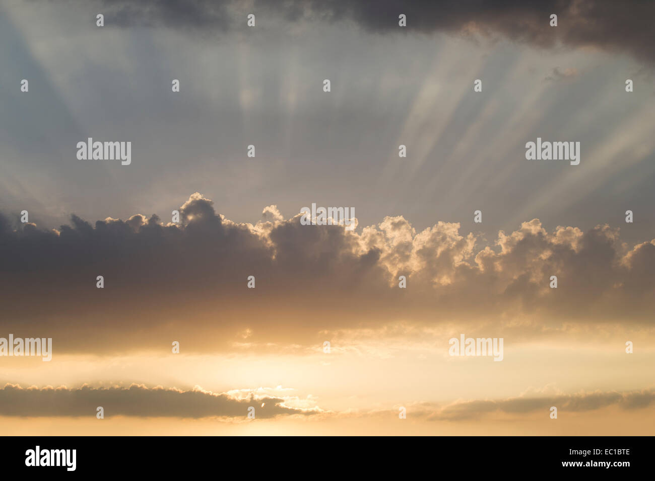 Crepuscular rays of light shining through clouds in the sky. Stock Photo