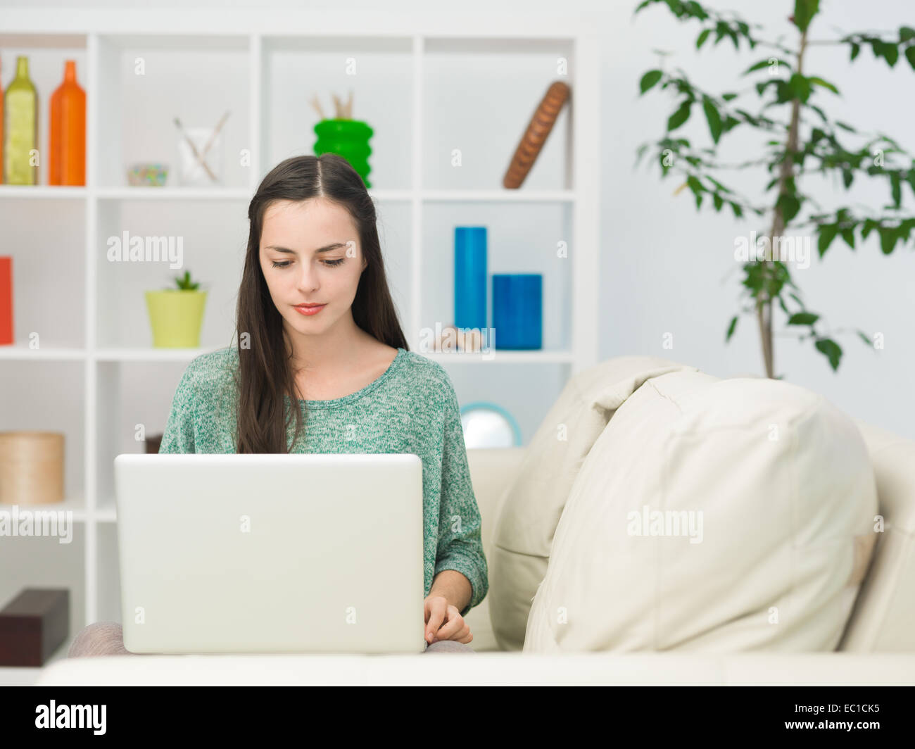 portrait of young beautiful woman sitting on sofa at home using laptop ...