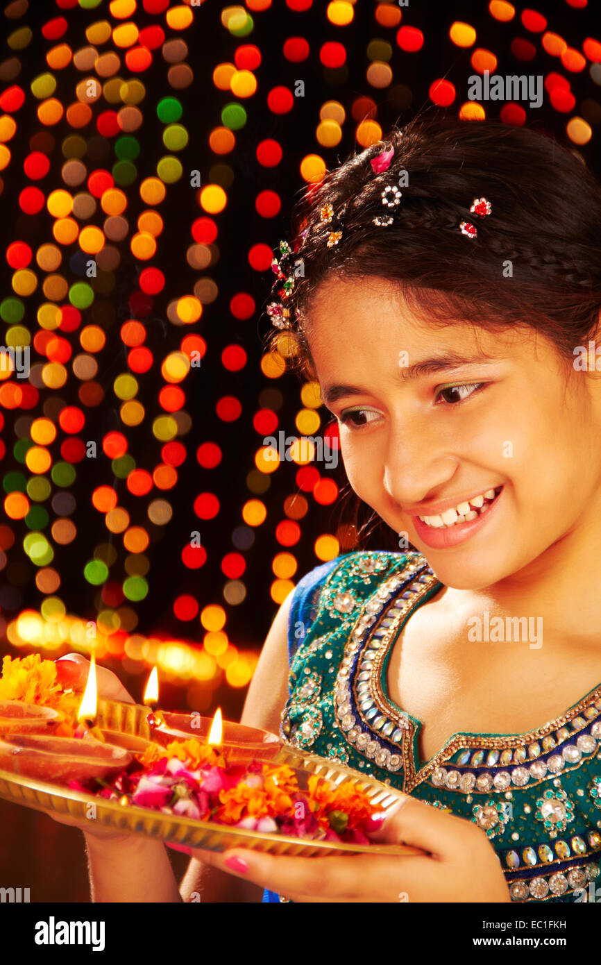 Image of An young and beautiful Indian Bengali woman in Indian traditional  dress is holding a Diwali diya/lamp in her hand in front of colorful bokeh  lights. Indian lifestyle and Diwali celebration-YI876738-Picxy