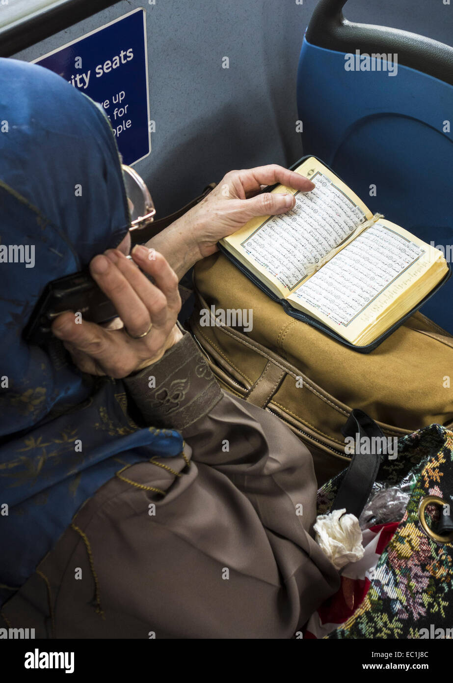Moslem woman studying Koran on London bus. (Qur'an or Koran). Answering a mobile phone with other hand. Stock Photo