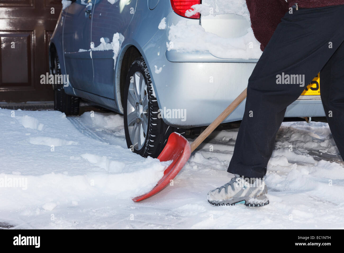 Person shoveling snow using a snow shovel to clear a car on path and