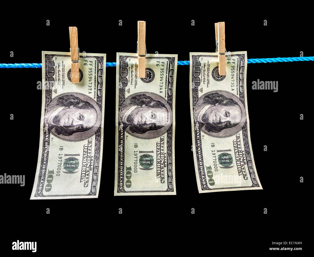 Three one hundred dollar banknotes hanging on laundry line attached with wooden clips over black background Stock Photo
