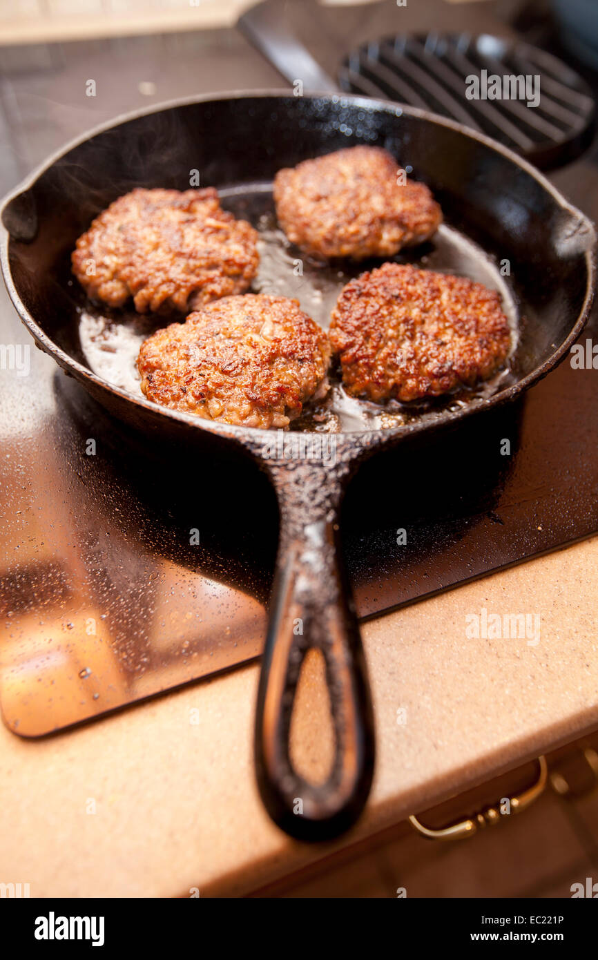 Hot sausage patties cooking in a black cast iron skillet on a stove top