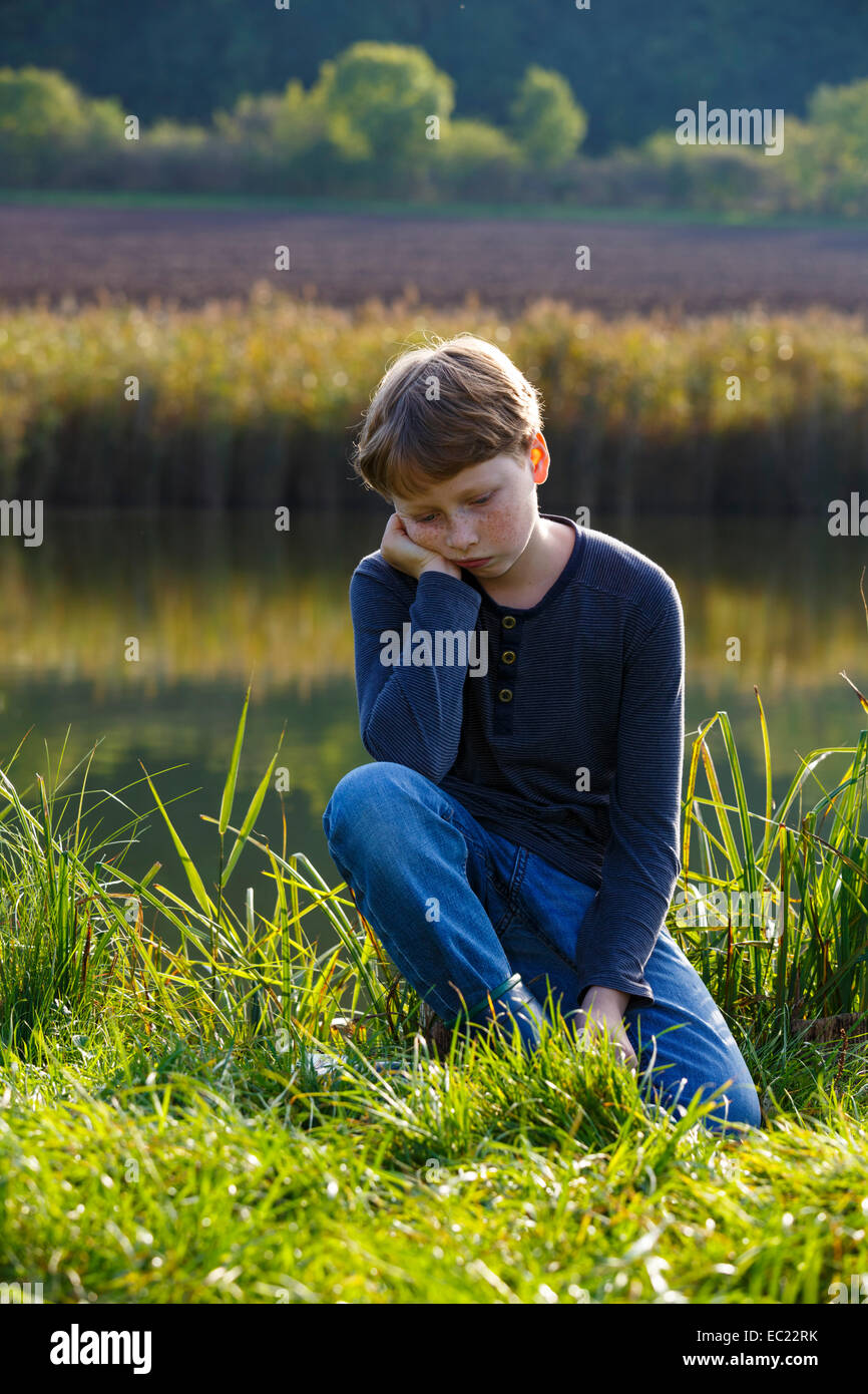 Sad boy sitting on a small lake, Wandersleben, Thuringia, Germany Stock Photo