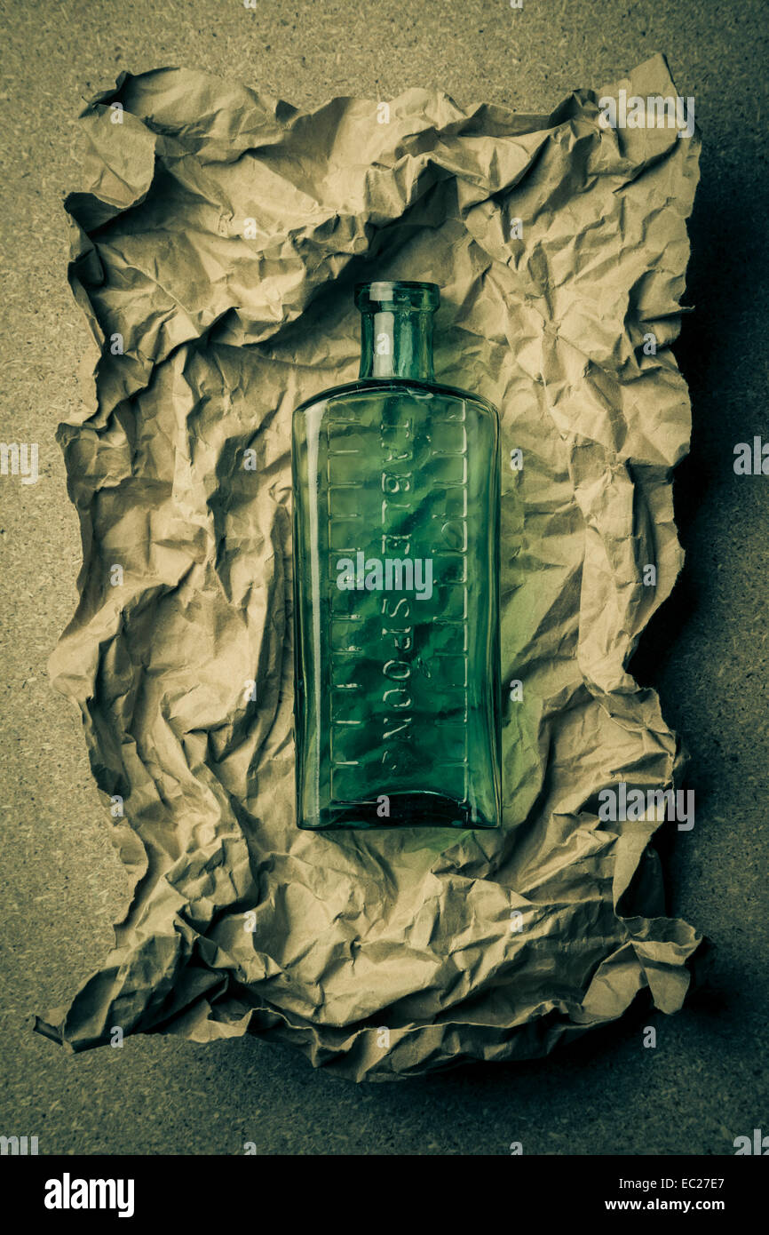 Blue green glass bottle on a crumpled paper background. Stock Photo