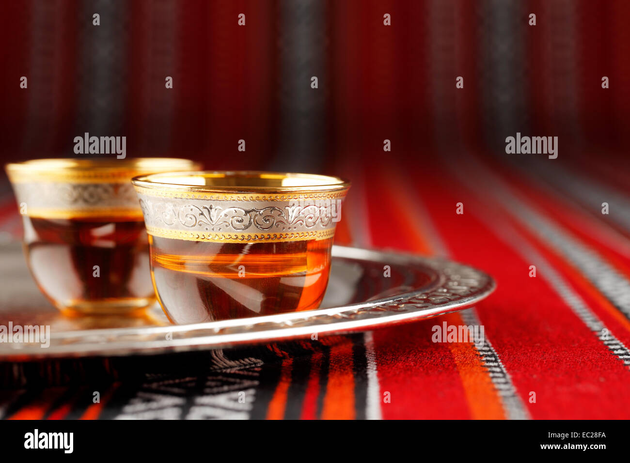 A tray of Arabian tea cups is placed on Arabian woven fabric. Tea symbolise Arabian hospitality Stock Photo