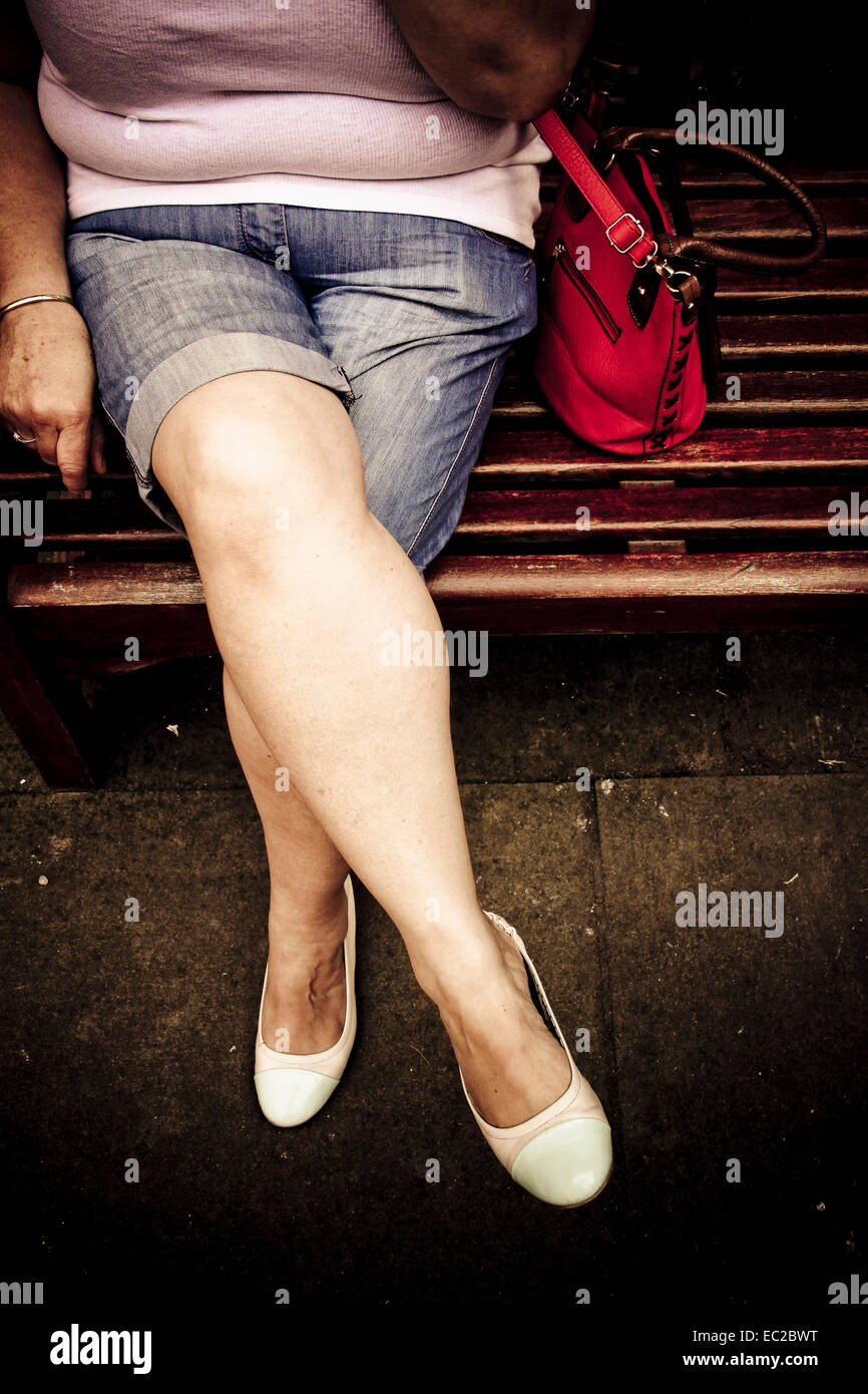 Middle aged woman's plump legs sitting on park bench Stock Photo
