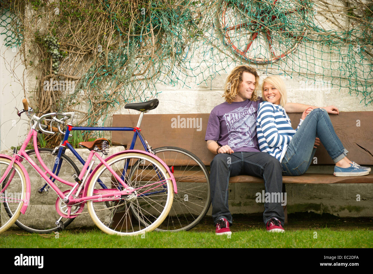 A young couple sat on a bench laughing Stock Photo