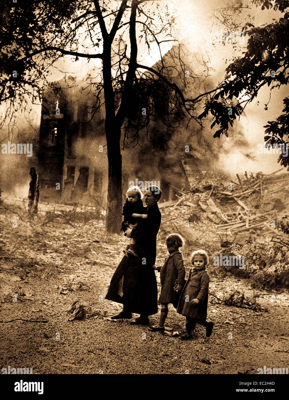 Belgian refugees flee combat as they walk past a bombed out home.  Circa 1940. Stock Photo
