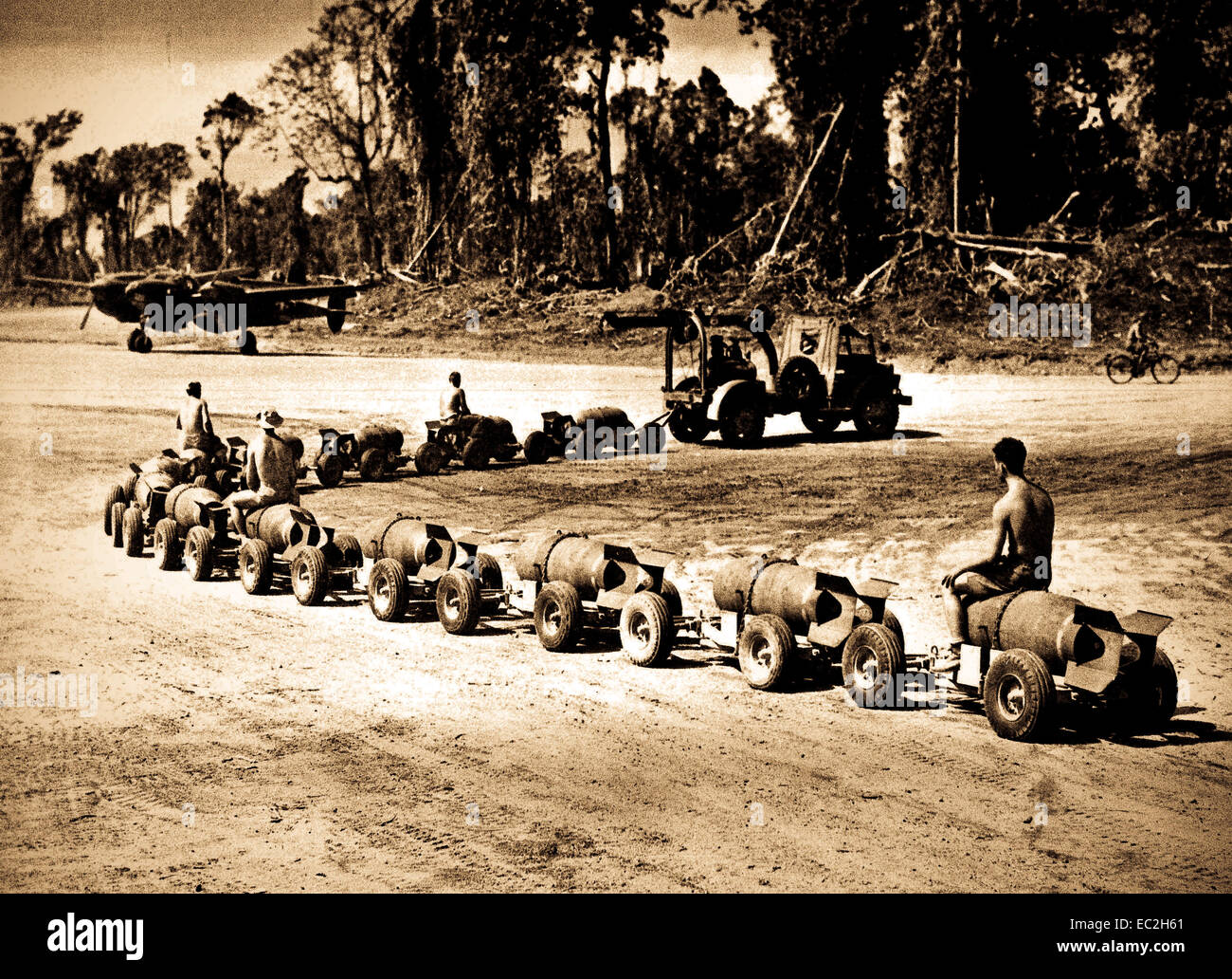 U.S. Navy sailors ride bombs as they are carted to waiting aircraft on a Pacific island Navy airfield during World War II . Stock Photo