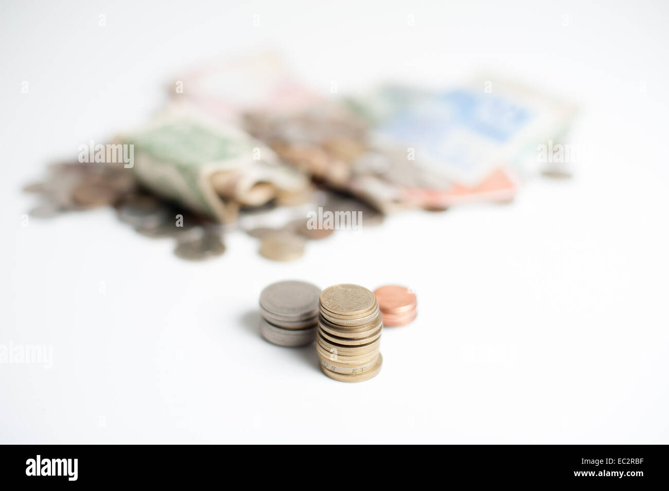 Three piles of coins, gold, silver, and bronze, with mountain of money coins and banknotes out of focus in background Stock Photo