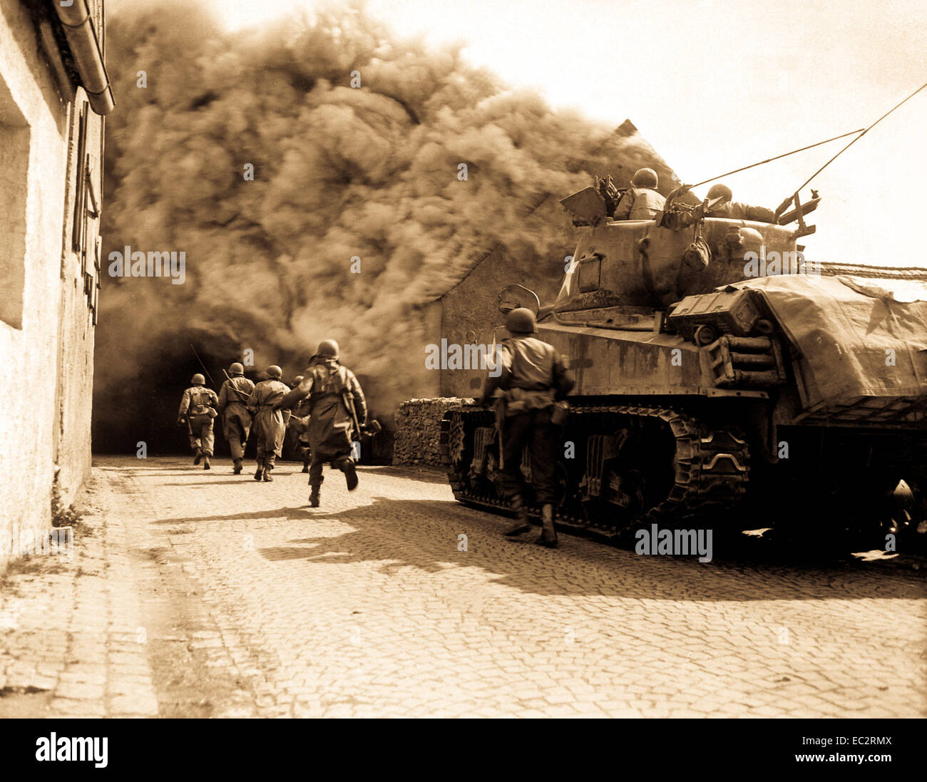 Soldiers of the 55th Armored Infantry Battalion and tank of the 22nd Tank Battalion, move through smoke filled street.  Wernberg, Germany.  April 22, 1945.  Pvt. Joseph Scrippens.  (Army) Stock Photo