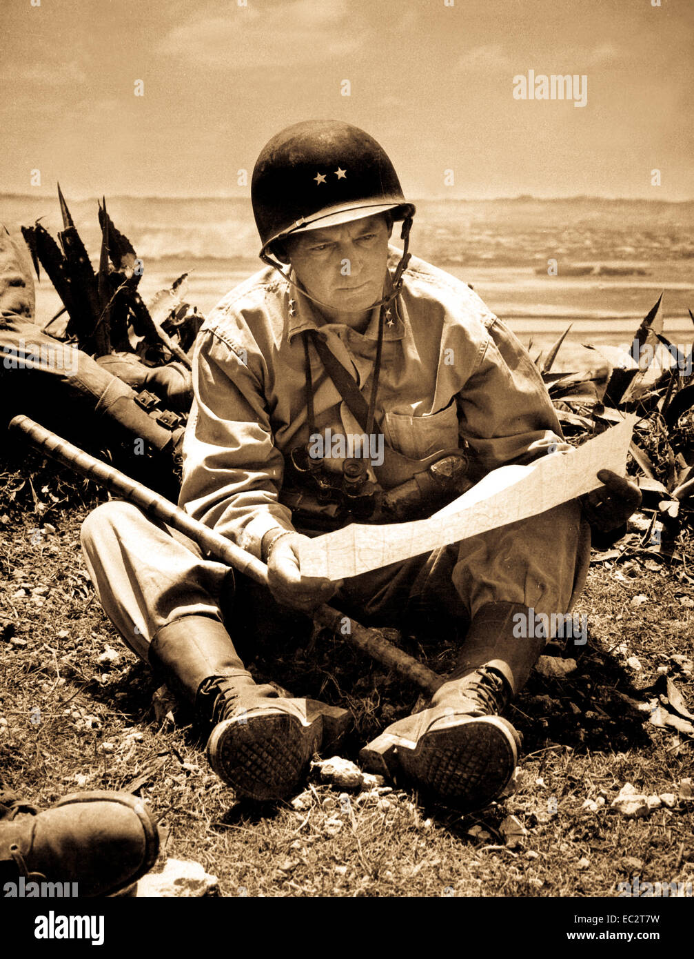 With the captured capital of Naha as a background, Marine Maj. Gen. Lemuel Shepherd, commanding general of the 6th Marine Division, relaxes on an Okinawan ridge long enough to consult a map of the terrain.  Ca. June 1945.  Pfc. Sam Weiner.   (Marine Corps) Stock Photo