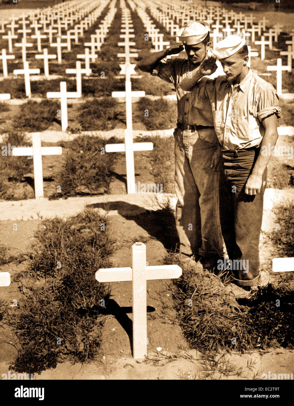 Standing in the grassy sod bordering row upon row of white crosses in an American cemetery, two dungaree-clad Coast Guardsmen pay silent homage to the memory of a fellow Coast Guardsman who lost his life in action in the Ryukyu Islands.  Ca. 1945. Benrud. (Coast Guard) Stock Photo