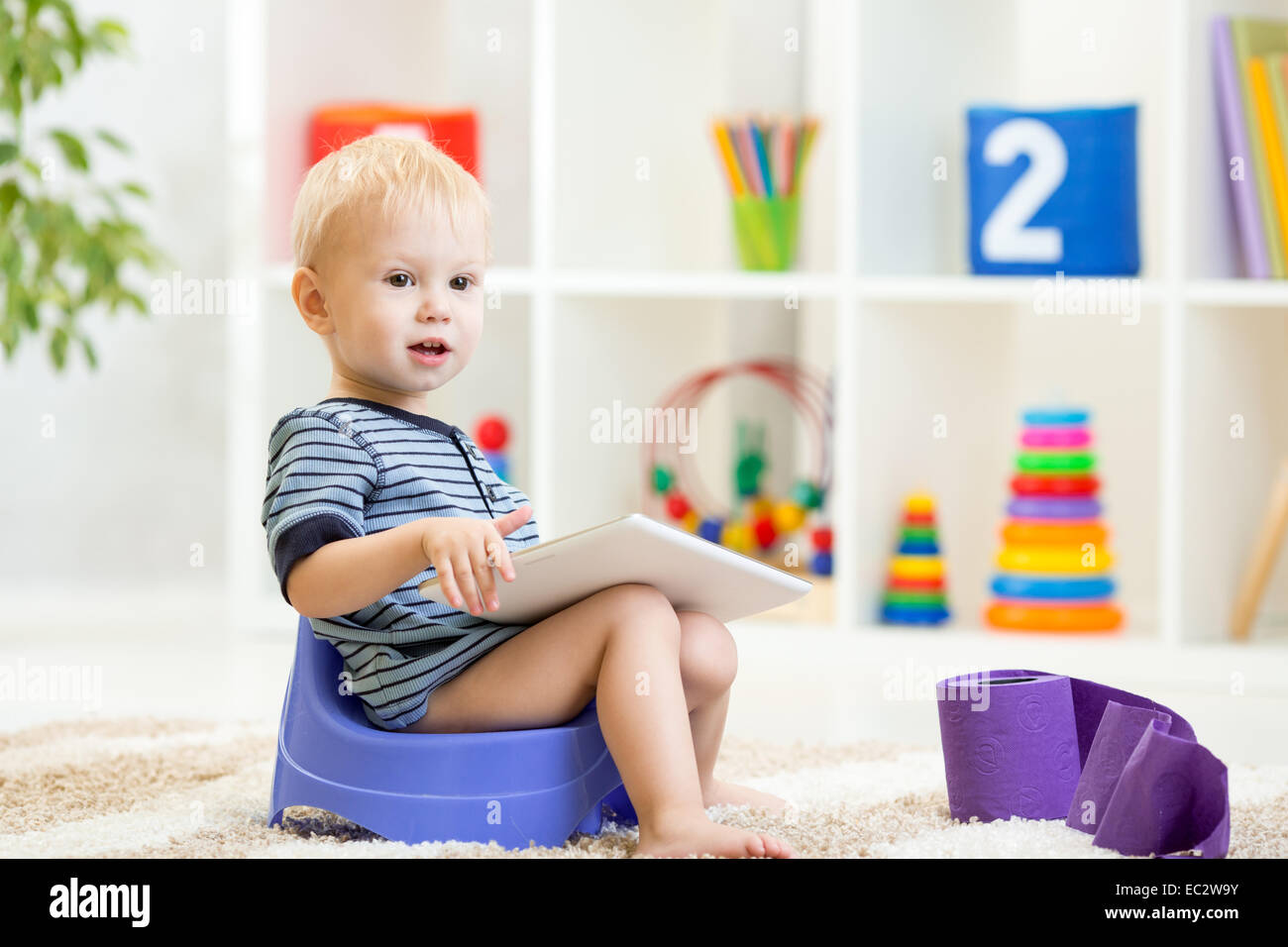toddler sitting on chamber pot playing tablet pc Stock Photo