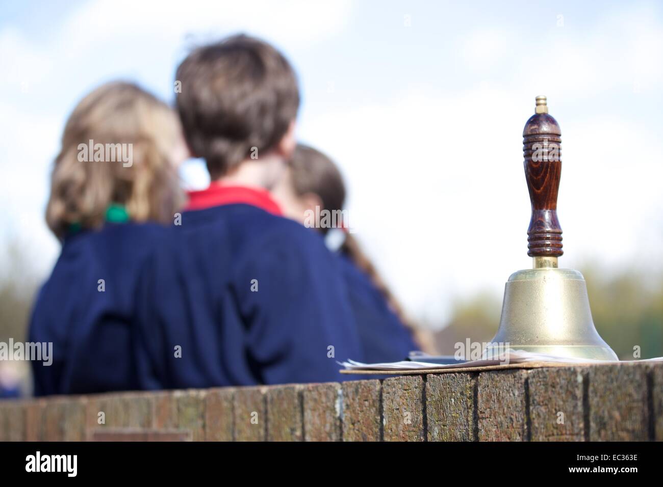 UK primary school playground with pupils in uniform in the background and a school hand bell in the foreground Stock Photo