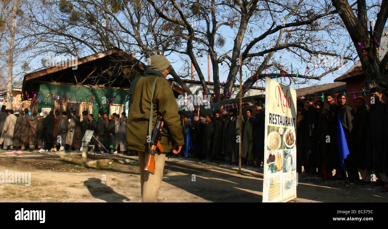 Srinagar, Indian Administered Kashmir. 9th December, 2014.  Indian central reserve police force ( CRPF) stands guard as  Kashmiri voters queue at a polling station in Beerwah on the outskirts of Srinagar.India-administered Kashmir headed to the third phase of state assembly polls under tight security with Indian Prime Minister Narendra Modi's Hindu nationalist party eyeing power for the first time in the tense and disputed Muslim-majority state. Credit:  sofi suhail/Alamy Live News Stock Photo
