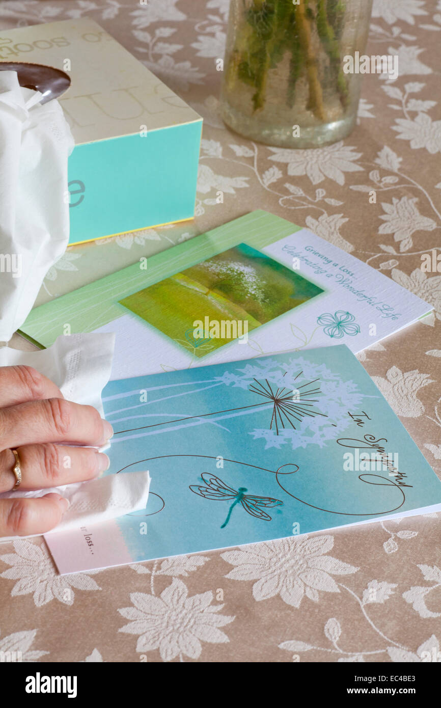 hand holding tissue with Sympathy cards and box of tissues on tablecloth Stock Photo