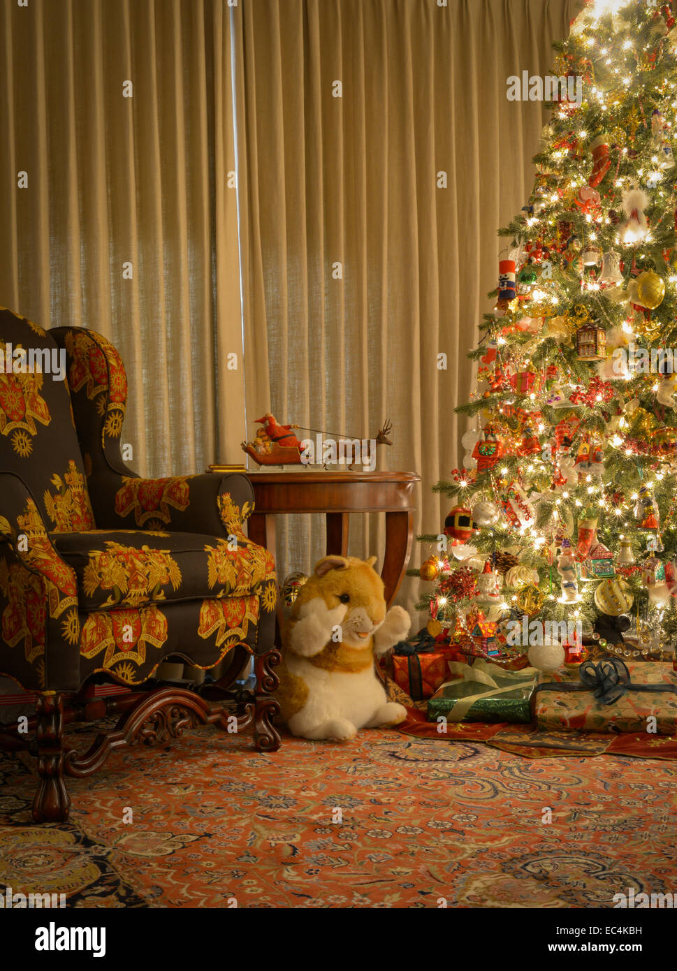 Heavily decorated Christmas tree with presents underneath next to chair Stock Image