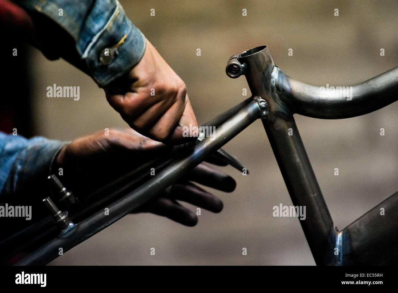 A bicycle worker grinds a recently welded bike frame in a small scale bicycle factory in Bogota, Colombia, 10 April 2013. Due to the strong, vibrant cycling culture in Colombia, with cycling being one of the two most popular sports in the country, dozens of bike workshops and artisanal, often family-run bicycle factories were always spread out through the Colombian cities. However, growing import of cheap bicycles and components from China during the last decade has led to a significant decline in domestic bicycle production. Traditional no-name bike manufacturers are forced to close down thei Stock Photo