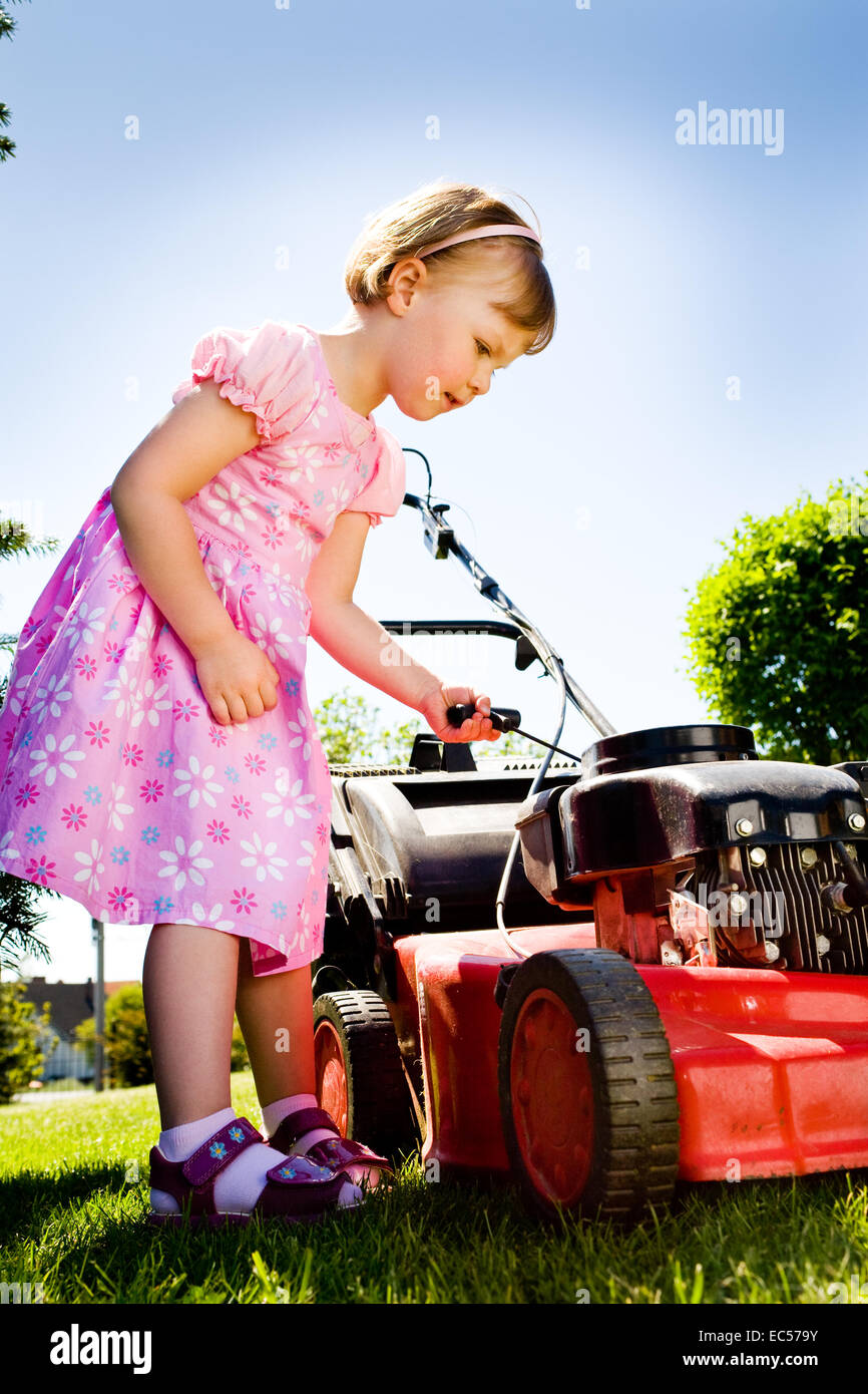 a 3,5 years old girl with lawnmower in the garden Stock Photo