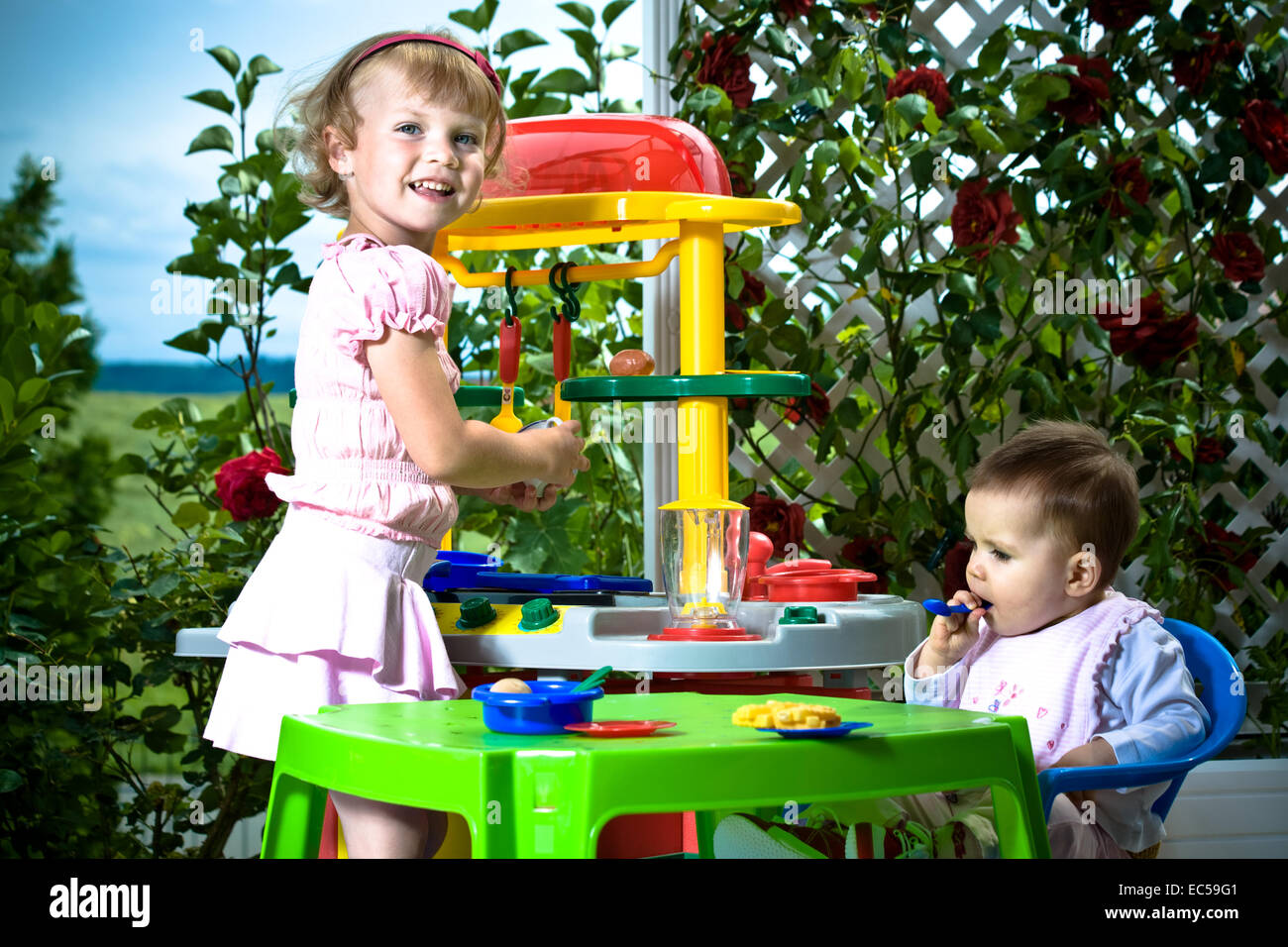 a 6 month old baby and a 4 years old girl in front of toy kitchen Stock Photo
