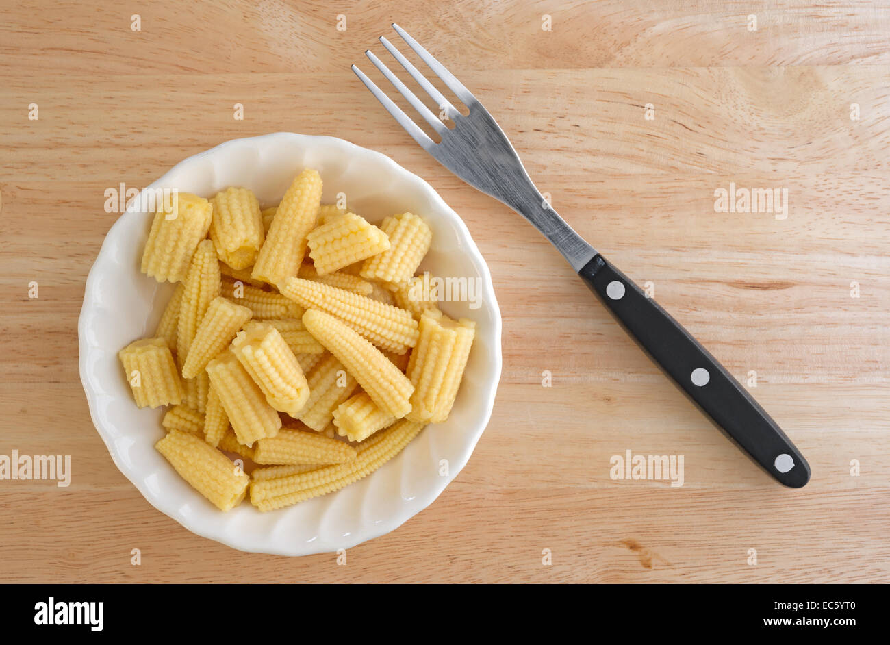 Top view of a bowl of corn nuggets in a small bowl with a fork to the side atop a wood table. Stock Photo