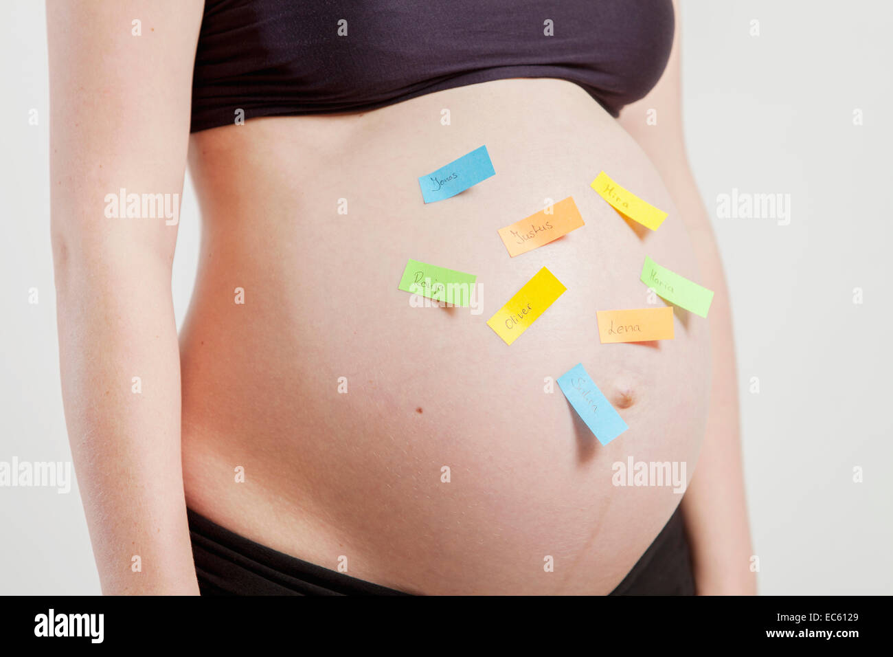 young pregnant woman with several Post Its where names are on it on your belly baby bump expectant mother Naming Undecided Stock Photo
