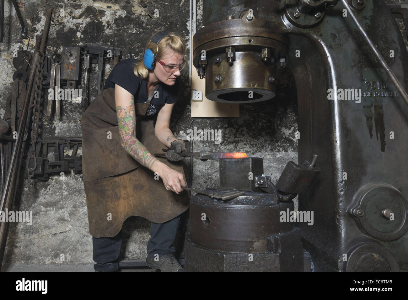 female blacksmith works a glowing piece of steel with steam hammer Stock Photo Alamy