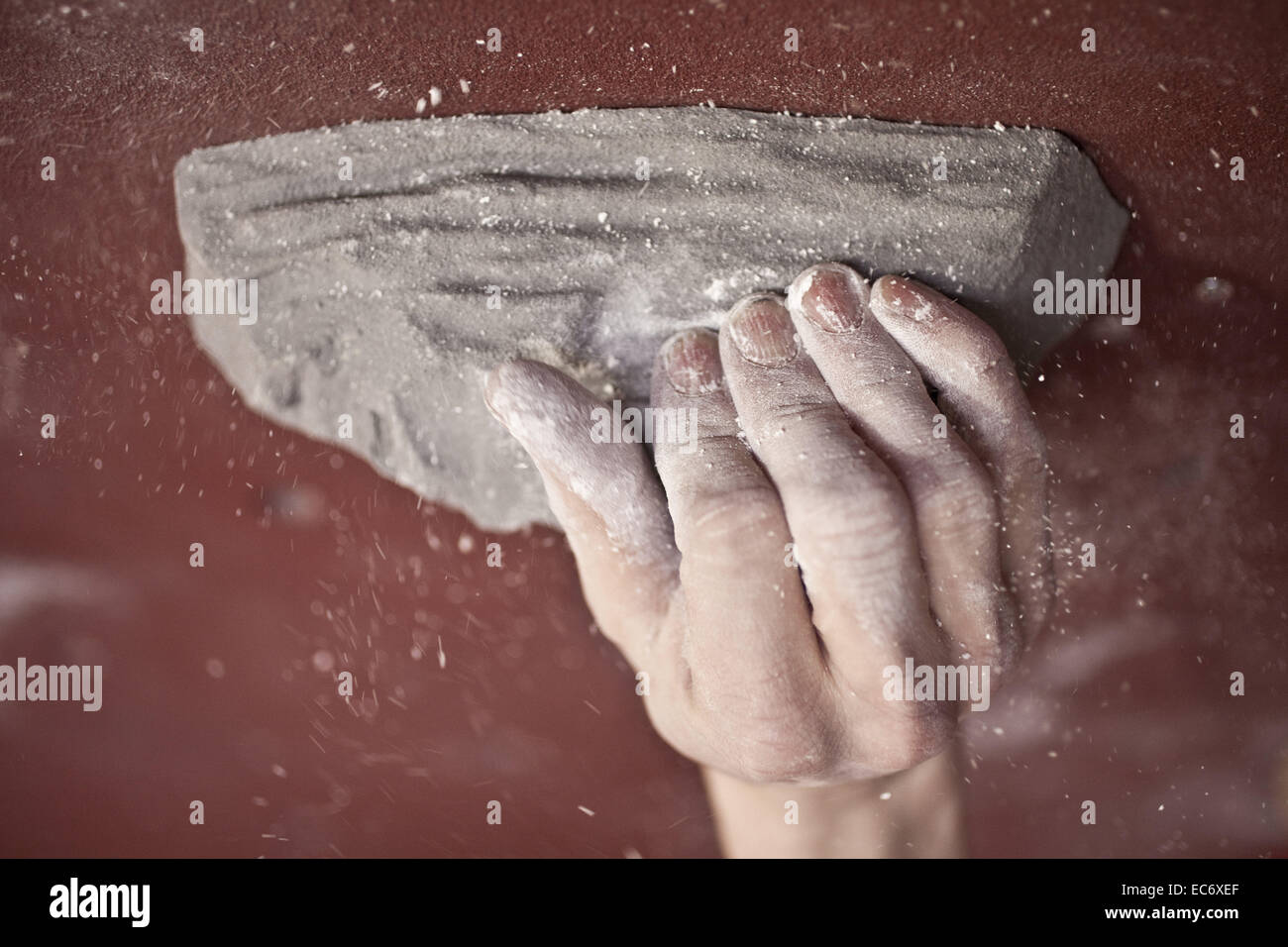 Climbers hand on a grip in a climbing hall, with chalk dust and red backround Stock Photo