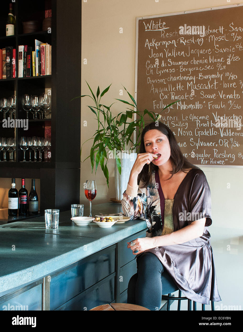 A woman sitting at a bar eating an olive and drinking a glass of wine. Stock Photo