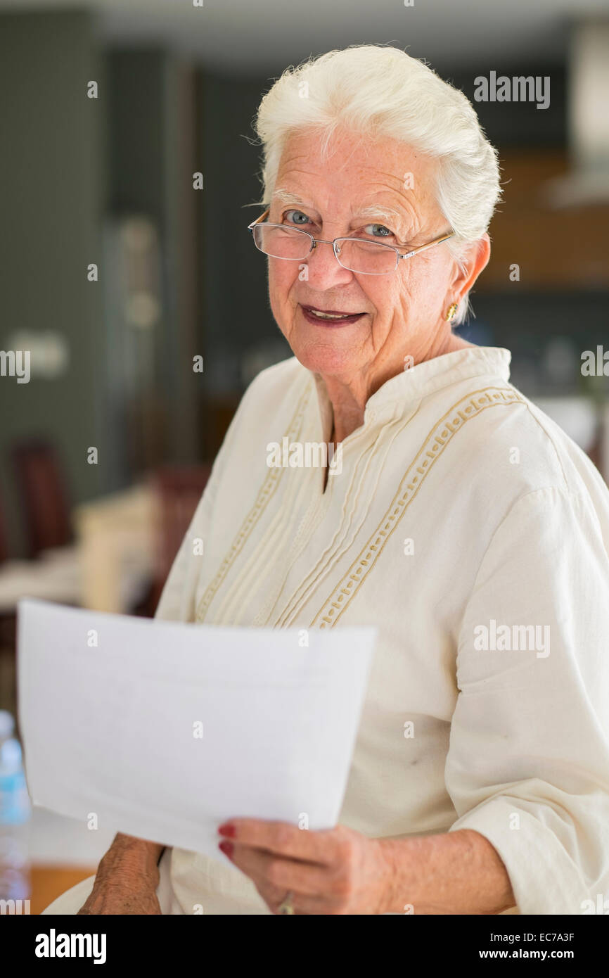 Portrait of smiling senior woman with glasses holding sheet of paper ...