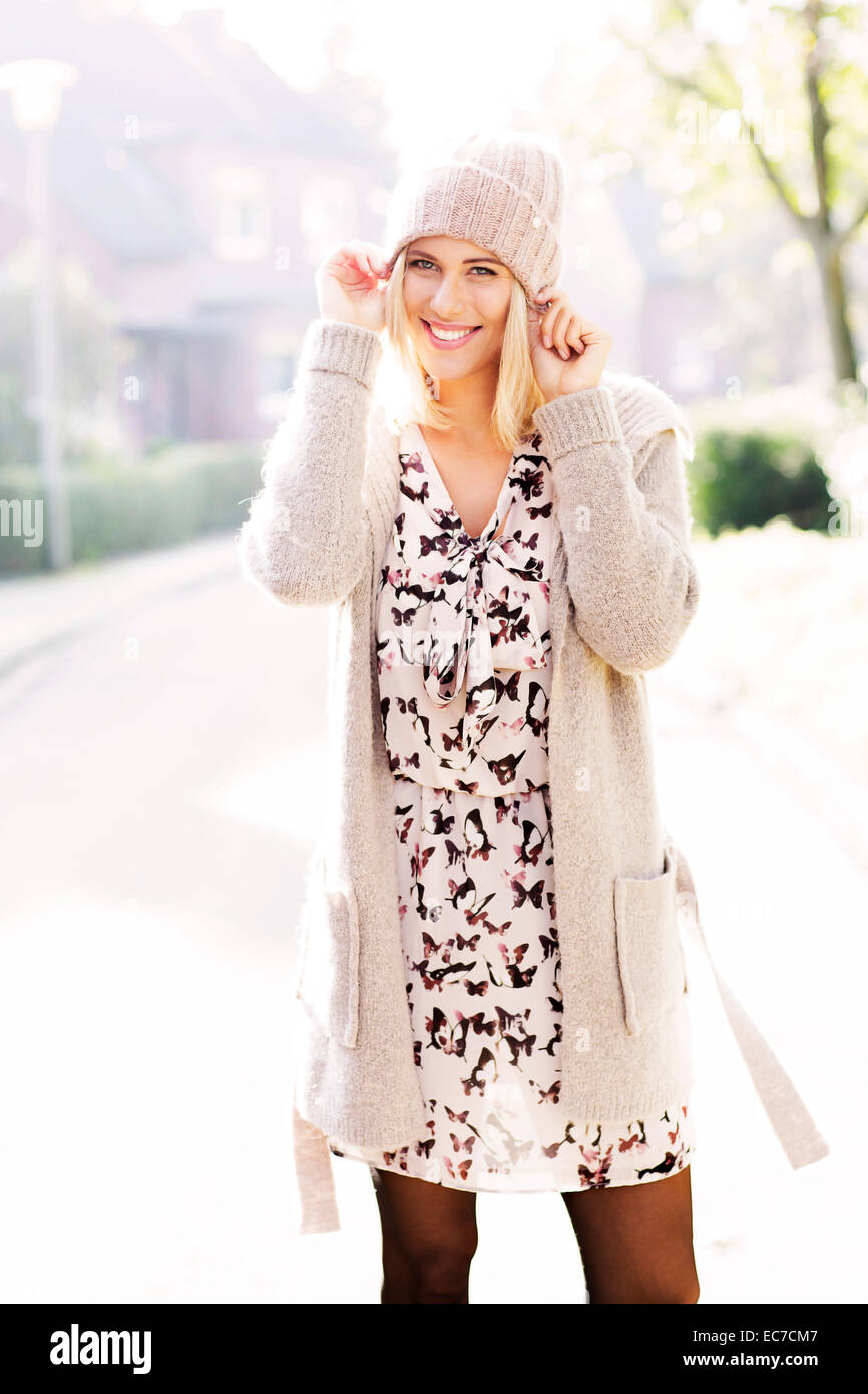 Portrait of smiling blond woman wearing patterned dress, cardigan and wool cap Stock Photo