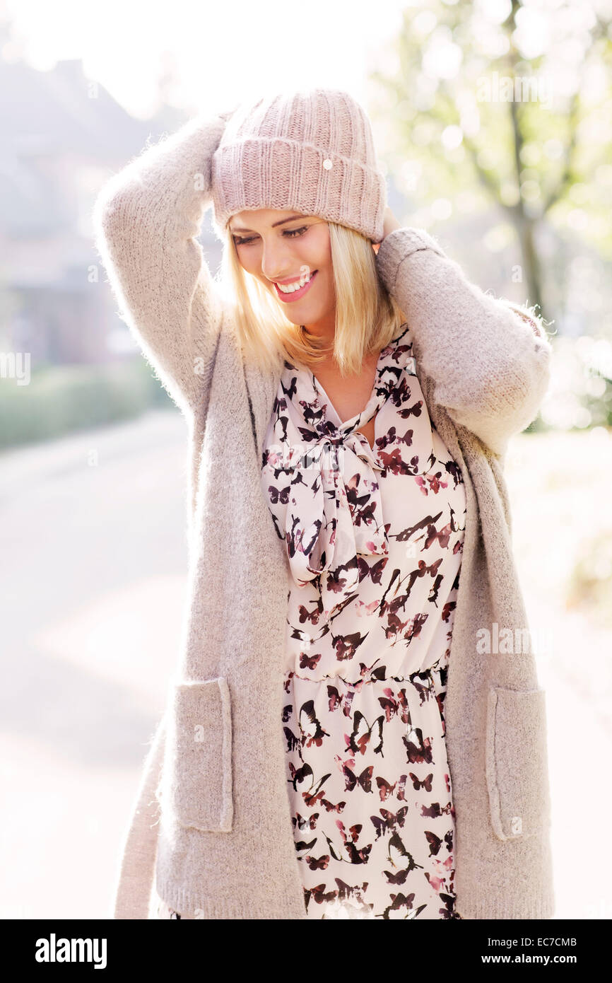 Smiling blond woman wearing patterned dress, cardigan and wool cap Stock Photo