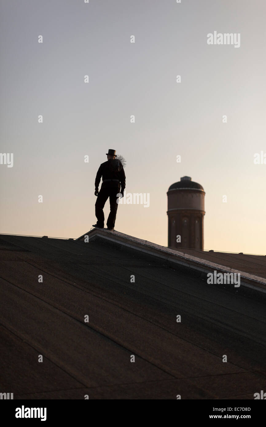 Germany, silhouette of chimney sweep standing on rooftop at twilight Stock Photo