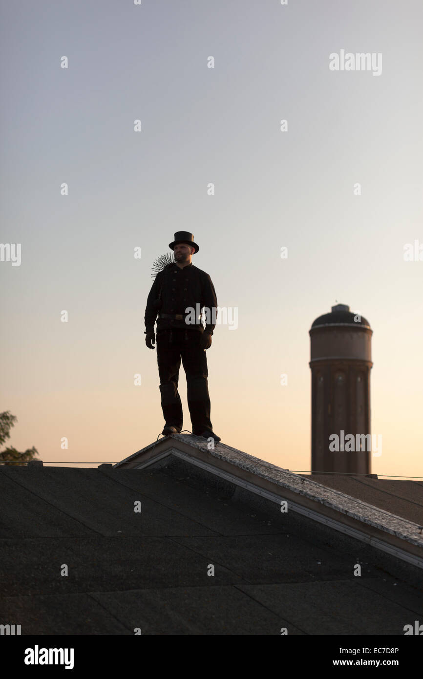 Germany, chimney sweep standing on rooftop at twilight Stock Photo